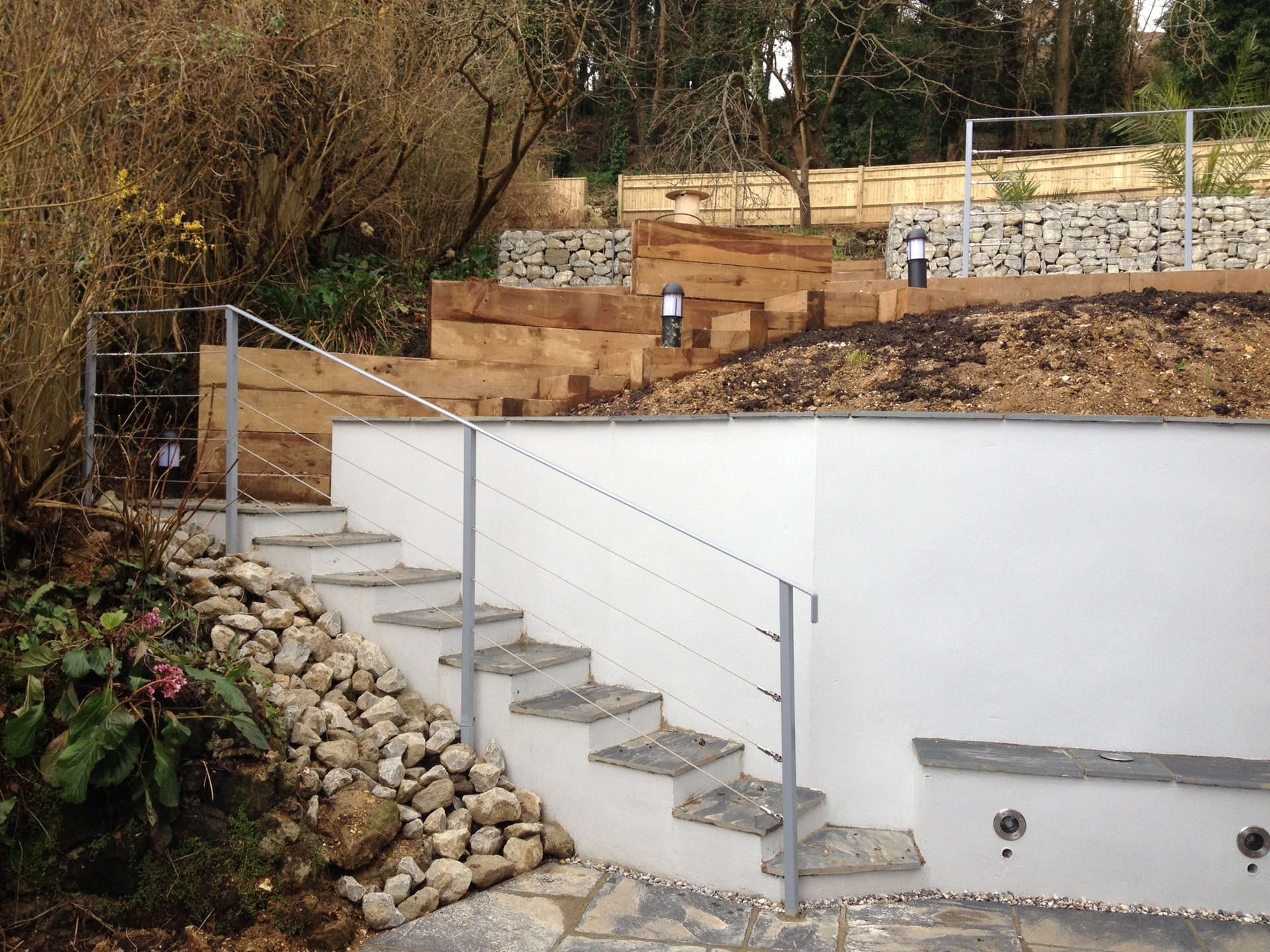 A sloping garden rebuilt with a rendered retaining wall, steps with a steel handrail and sleeper terraces