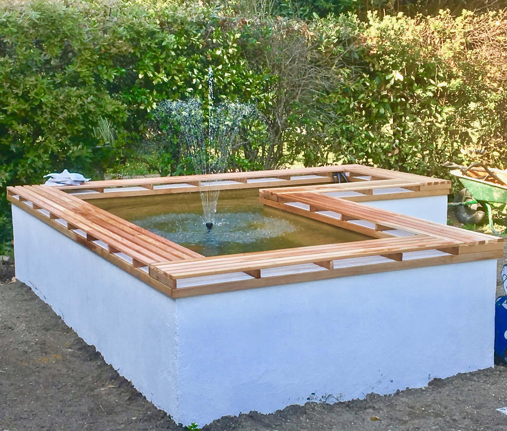 A raised rendered pond with a timber seating edge and a fountain